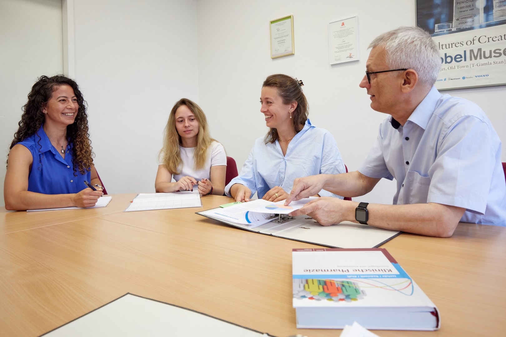 Eine Wissenschaftlerin und ein Wissenschaftler arbeiten hinter einer Glasfassade und mischen Chemikalien mit Großgeräten.