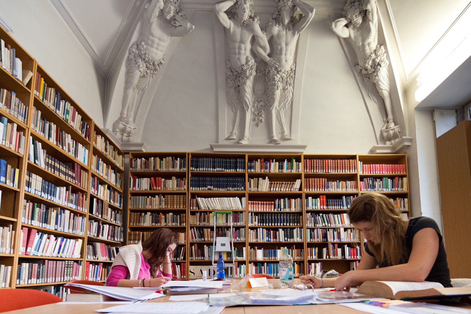 Eine Wissenschaftlerin und ein Wissenschaftler arbeiten hinter einer Glasfassade und mischen Chemikalien mit Großgeräten.